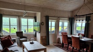 A cozy room with a sofa, a dining table, and chairs, large windows with curtains, and a wooden ceiling. - Myrkdalen stay (Myrkdalen)