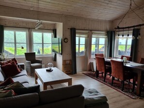 A cozy room with a sofa, a dining table, and chairs, large windows with curtains, and a wooden ceiling. - Myrkdalen stay (Myrkdalen)