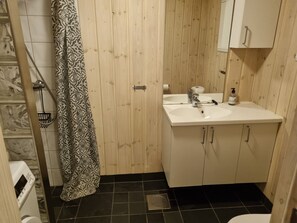 A bathroom with a wooden door, a sink with a mirror, a toilet, and a shower curtain. - Vrbo Property (Myrkdalen)