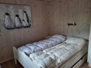 Un letto singolo con materasso e cuscini bianchi, una parete in legno con un quadro e un comodino.