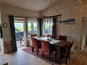 Un interno in legno con un tavolo da pranzo, sedie, un tappeto e vista attraverso la porta in vetro.