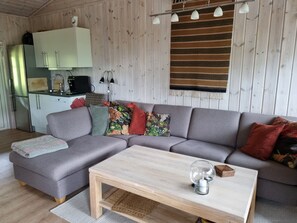 A modern living room with a grey sectional sofa, a wooden coffee table, and a kitchen area with white cabinets and a stainless steel refrigerator. - Vrbo Property (Myrkdalen)