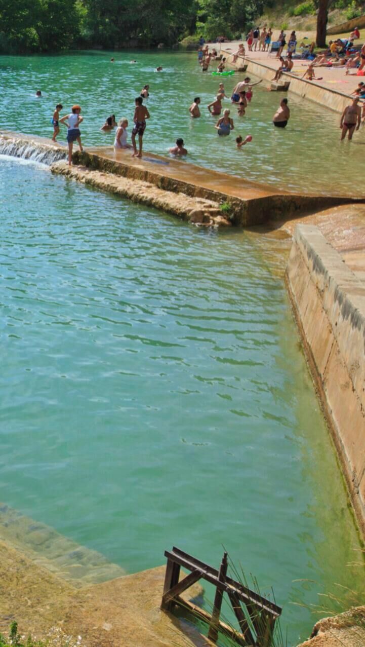 Une zone de baignade où l’on voit des personnes dans l’eau et au bord, le tout étant entouré d’une structure en béton.