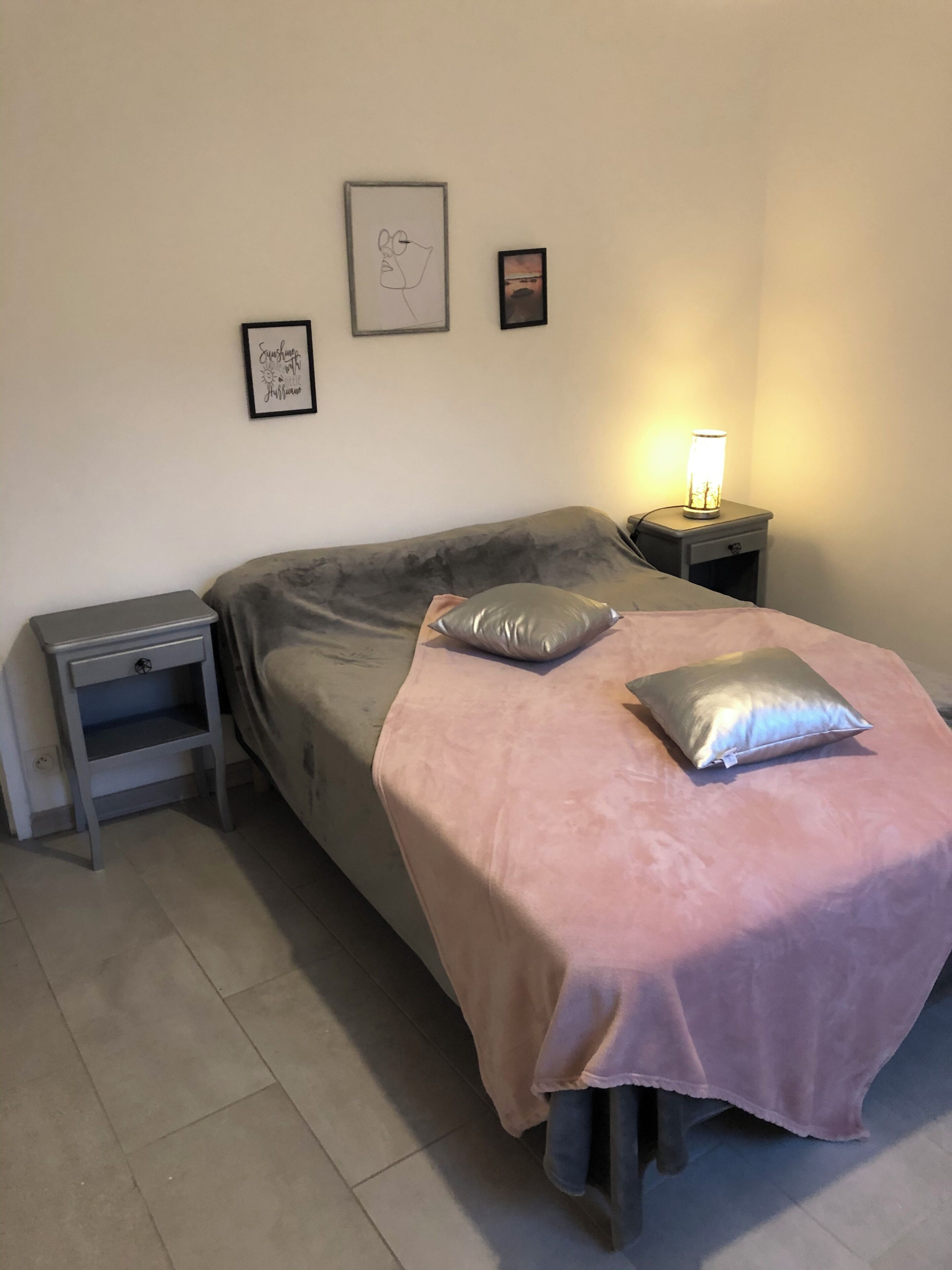 Une chambre à coucher avec un lit, une table de chevet, une lampe et des œuvres d’art murales.