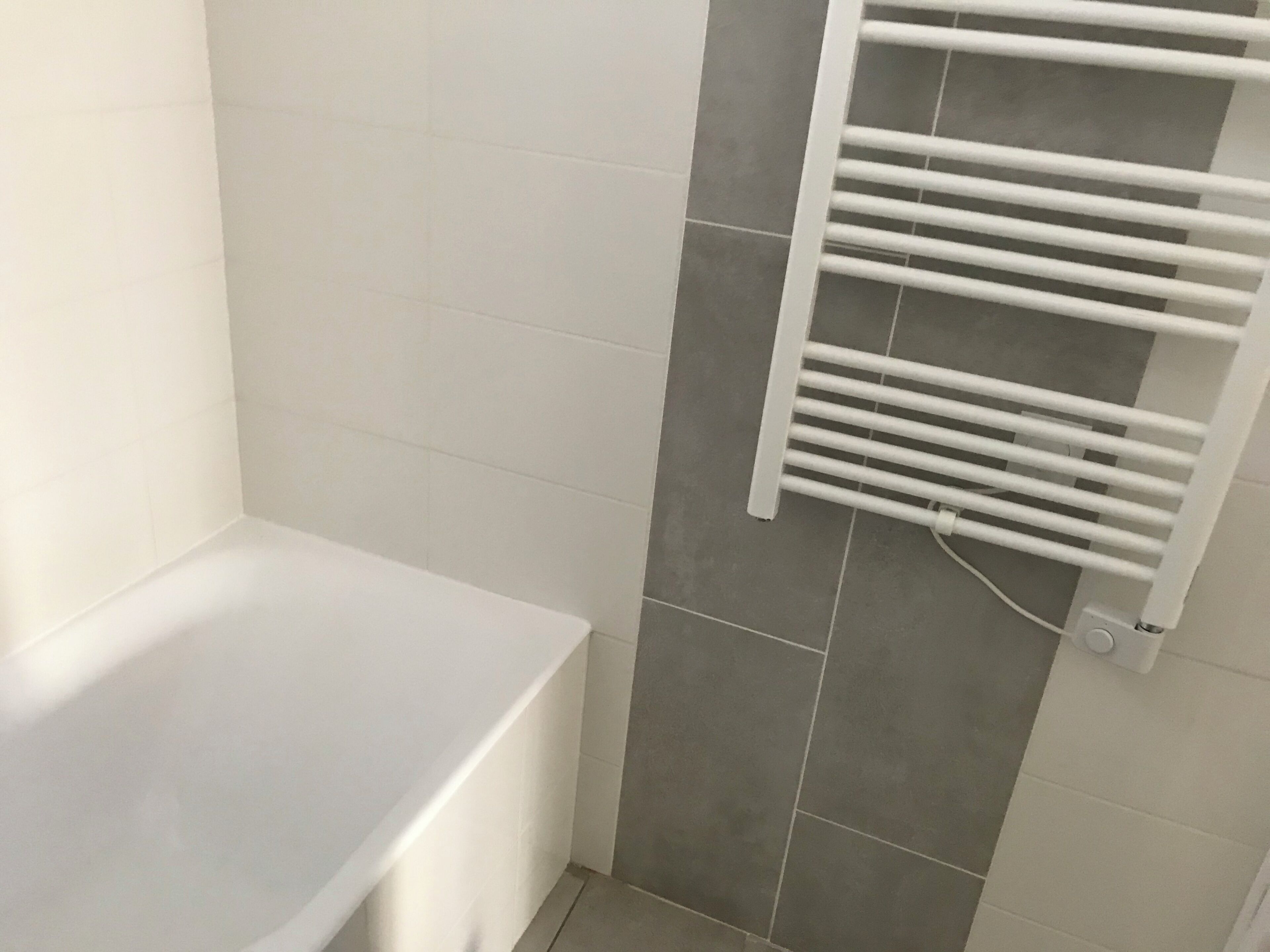 A bathroom with a white bathtub, a white towel rack, and grey tiles.