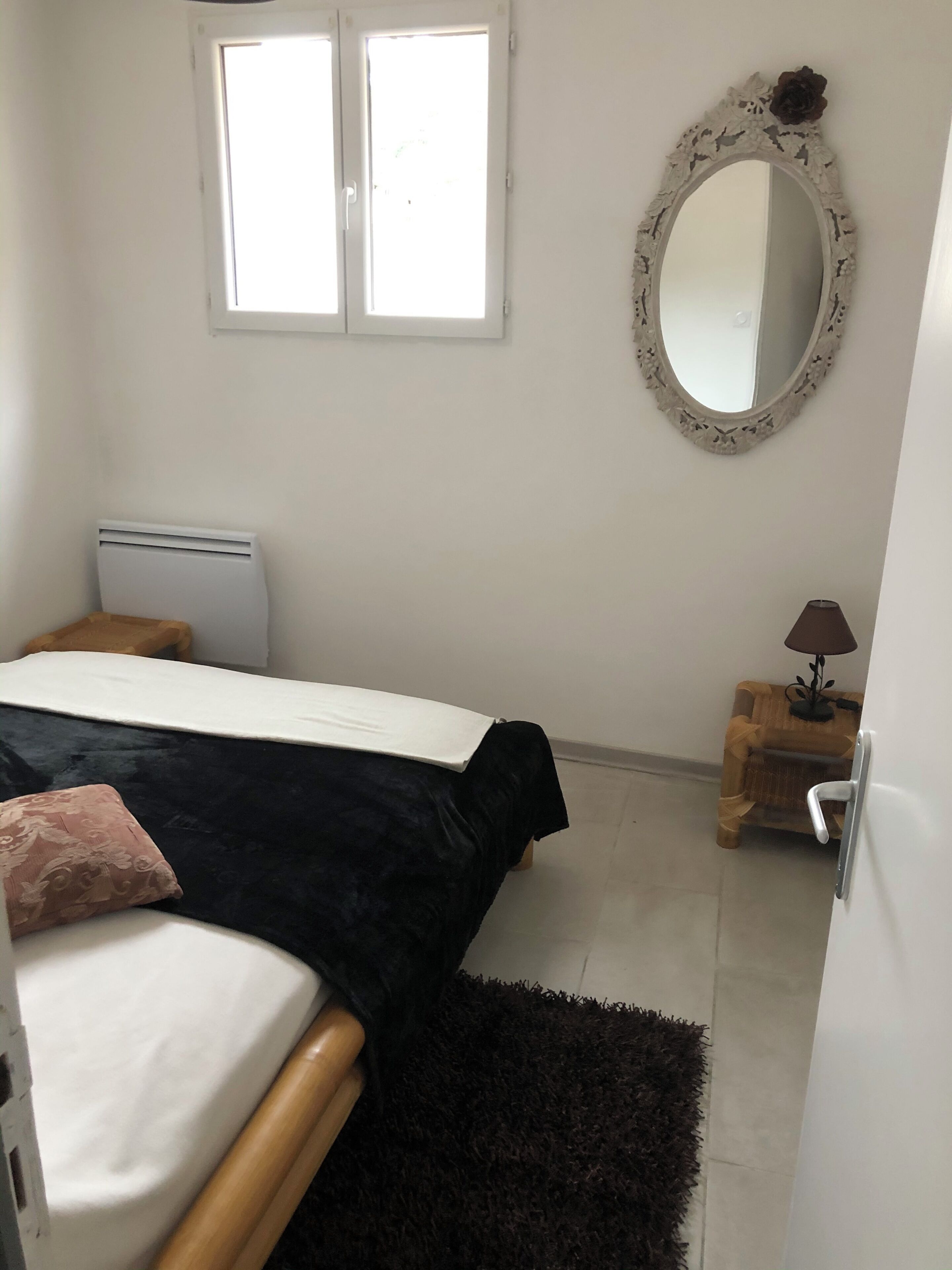 Un dormitorio con cama, mesita de noche, lámpara, espejo y ventana.
