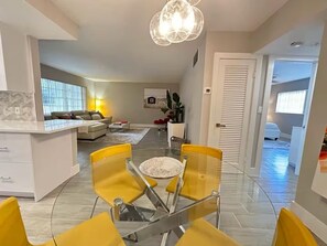 A modern living room with a sofa, a dining table with yellow chairs, a kitchen area, and a hallway leading to a bedroom. - Gorgeous1BED Beach Walk distance in Fort Lauderdale (Fort Lauderdale)