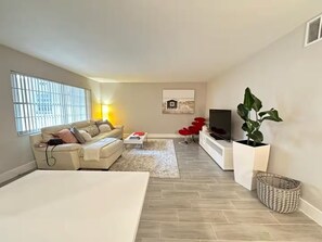 Un salon avec un canapé, une table basse, un téléviseur et une grande plante.