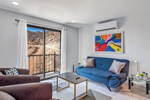 Uma sala de estar moderna com um sofá azul, uma mesa de centro e uma janela grande com vista para as montanhas.