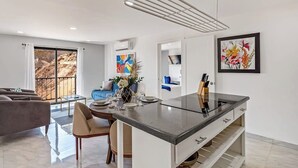 A modern kitchen with a central island, dining area with a table and chairs, and a living room with a sofa and a large window. - Morgan Residences 508 @ Boutique Hotel With Pool, Gym & Spa (Cabo San Lucas)