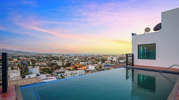 An infinity pool with a cityscape view, a white building with satellite dishes, and a clear sky. - Morgan Residences 508 @ Boutique Hotel With Pool, Gym & Spa (Cabo San Lucas)