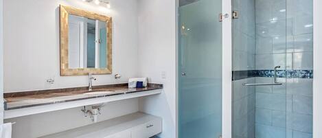 Un baño moderno con cabina de ducha de vidrio, tocador con espejo y encimera de mármol.
