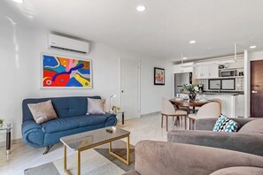 Uma sala de estar moderna com um sofá azul, uma mesa de centro e uma área de jantar com uma mesa e cadeiras.