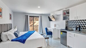 A bedroom with a bed, a desk, and a kitchen area with a dishwasher and microwave. - Morgan Residences 508 @ Boutique Hotel With Pool, Gym & Spa (Cabo San Lucas)