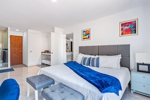Ein modernes Schlafzimmer mit einem großen Bett, einem Nachttisch, einem Kleiderschrank und einem durch eine geöffnete Tür einsehbaren Badezimmer.