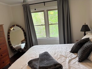 Ein Schlafzimmer mit einem Bett, einem Schminktisch, einem Spiegel, einem Fenster mit Vorhängen und einer Lampe.