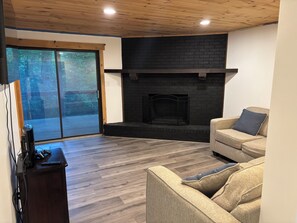 Ein Wohnzimmer mit Kamin, Holzboden, einer Couch und einem Fernsehschrank.