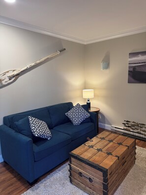 A living room with a blue sofa, patterned pillows, a wooden coffee table, a lamp, and a wall-mounted fish decoration. - Suite 3 for the win! Secluded suite overlooking the harbour, Spectacular views (Thetis Island)
