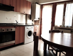 Eine Küche mit Waschmaschine, Esstisch und einem fenster mit Vorhängen.