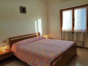 Ein Schlafzimmer mit Bett, Nachttischlampe und einem Fenster mit Spitzenvorhängen.