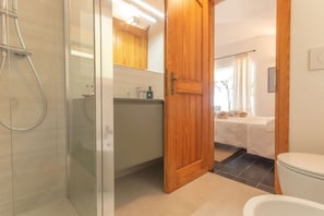 Ein Badezimmer mit Duschkabine aus Glas, einer Holztür, einer weißen Toilette und einem Waschbecken mit Spiegel darüber.