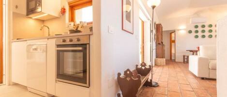 A compact kitchen with a microwave, oven, and dishwasher, a hallway with a crown-shaped decoration, and a living area with a white sofa.