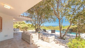 Um pátio externo com mobiliário, piscina e vista para o mar.