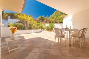 Eine Terrasse im Freien mit Tisch und Stühlen, einem kleinen weißen Hocker und einer Vase mit Blumen.
