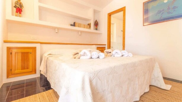 Quarto com cama, armário de madeira, espelho e prateleira com livros e figuras.