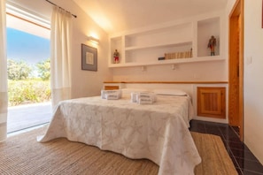 Ein Hotelzimmer mit einem Bett, einem großen Fenster mit Vorhängen, einem Regal mit Büchern und Figuren sowie einem kleinen Holzschrank.