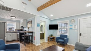 A modern living room with a kitchen, a blue armchair, a grey sofa, and a flat-screen TV. - Sunny Side Up - Heart of Folly Two Bedroom Stay (Folly Beach)
