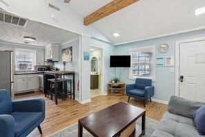 A modern living room with a kitchen, a blue armchair, a grey sofa, and a flat-screen TV. - Sunny Side Up - Heart of Folly Two Bedroom Stay (Folly Beach)