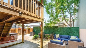 A wooden deck with a swing, wicker furniture, and a green hedge. - Sunny Side Up - Heart of Folly Two Bedroom Stay (Folly Beach)