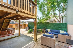 A wooden deck with a swing, wicker furniture, and a green hedge. - Sunny Side Up - Heart of Folly Two Bedroom Stay (Folly Beach)