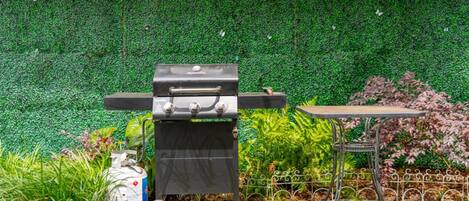 A barbecue grill with a table and a decorative fence in a garden setting.