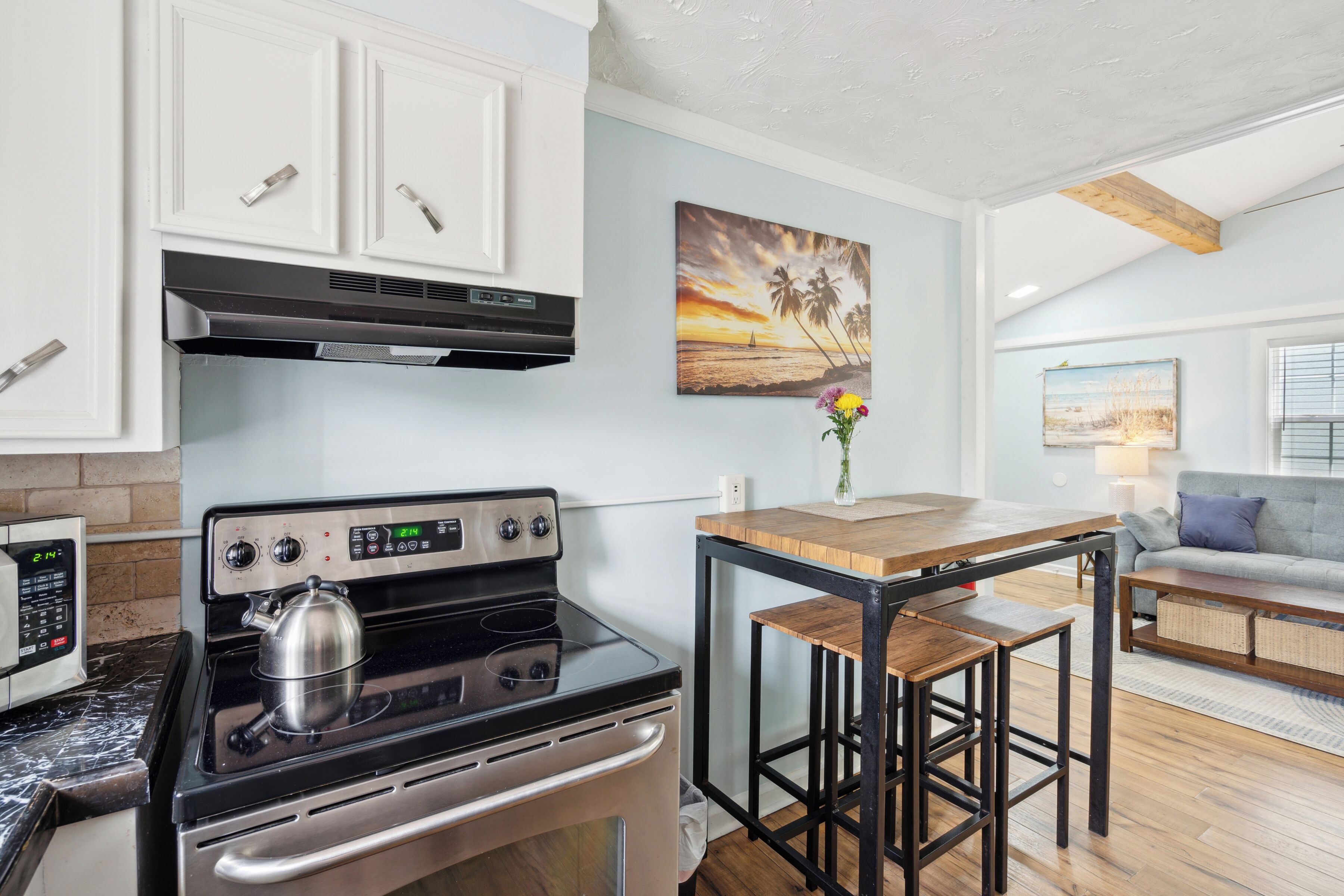 A kitchen with a stove, cabinets, and a painting of a sunset.