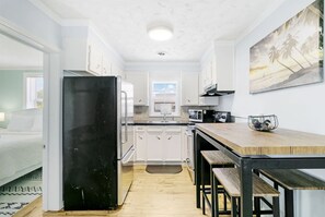A compact kitchen with white cabinets, a black refrigerator, a microwave, and a wooden dining table. - Heart of Folly Beach: Walk Everywhere, Sleeps 5 (Folly Beach)