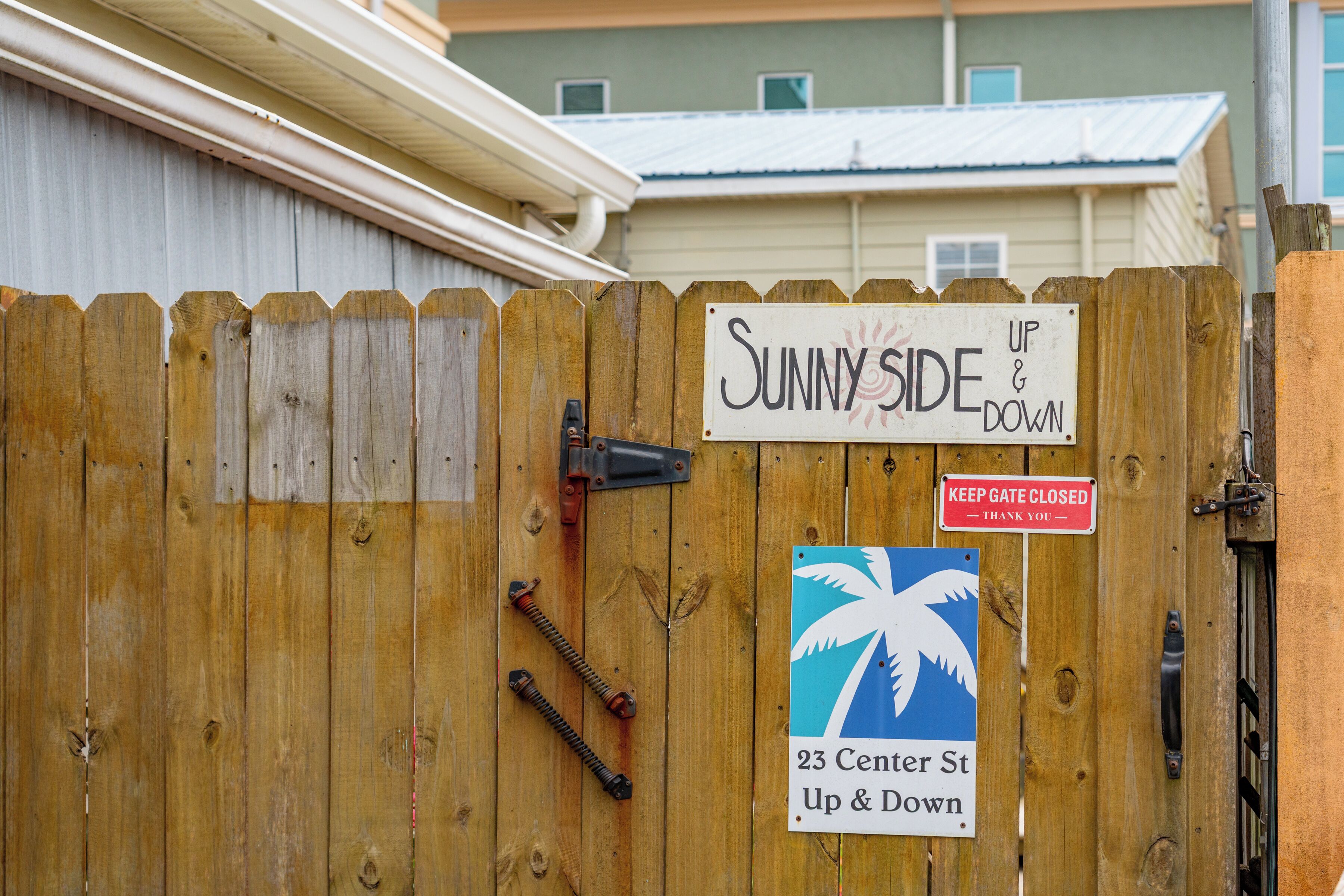 A wooden fence with signs reading 'Sunny Side Up & Down' and 'Keep Gate Closed - Thank You.'