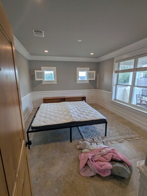Un dormitorio con una cama, dos ventanas con contraventanas, un radiador y una puerta.