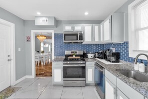 A modern kitchen with stainless steel appliances, a blue tiled backsplash, and white cabinetry. - Perfect 4-bedroom house with EV Charger in pleasant Buffalo neighborhood (Buffalo)