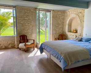 Ein Schlafzimmer mit Steinwand, einem Bett mit blauer Bettwäsche, einem Holzstuhl und einem großen Fenster.