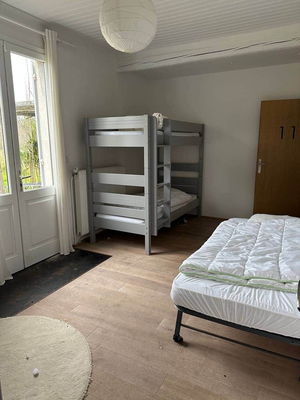 A room with bunk beds, a single bed, a wooden door, and a window with curtains.