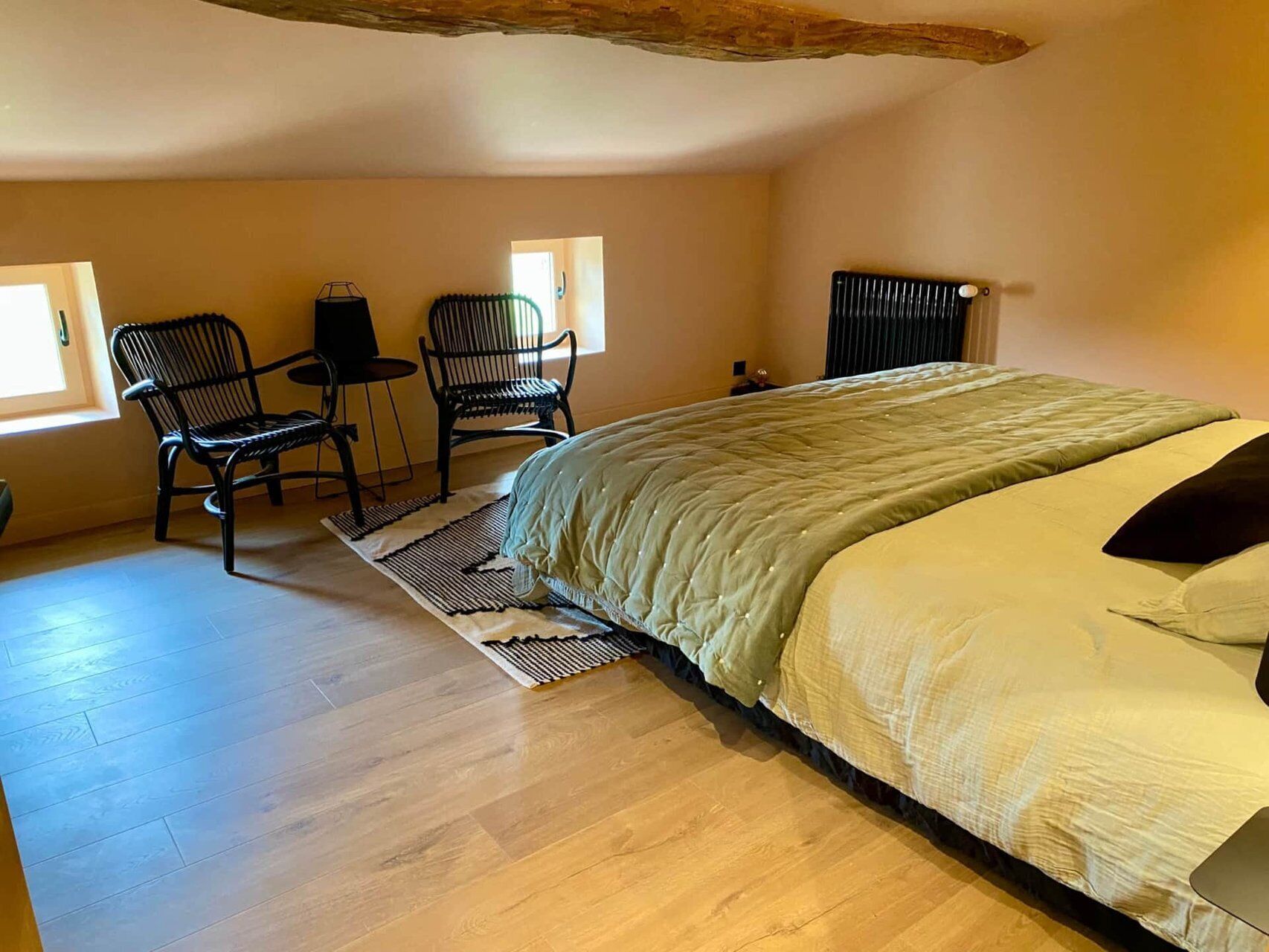 Een slaapkamer met een bed, twee stoelen, een bijzettafeltje en een radiator.