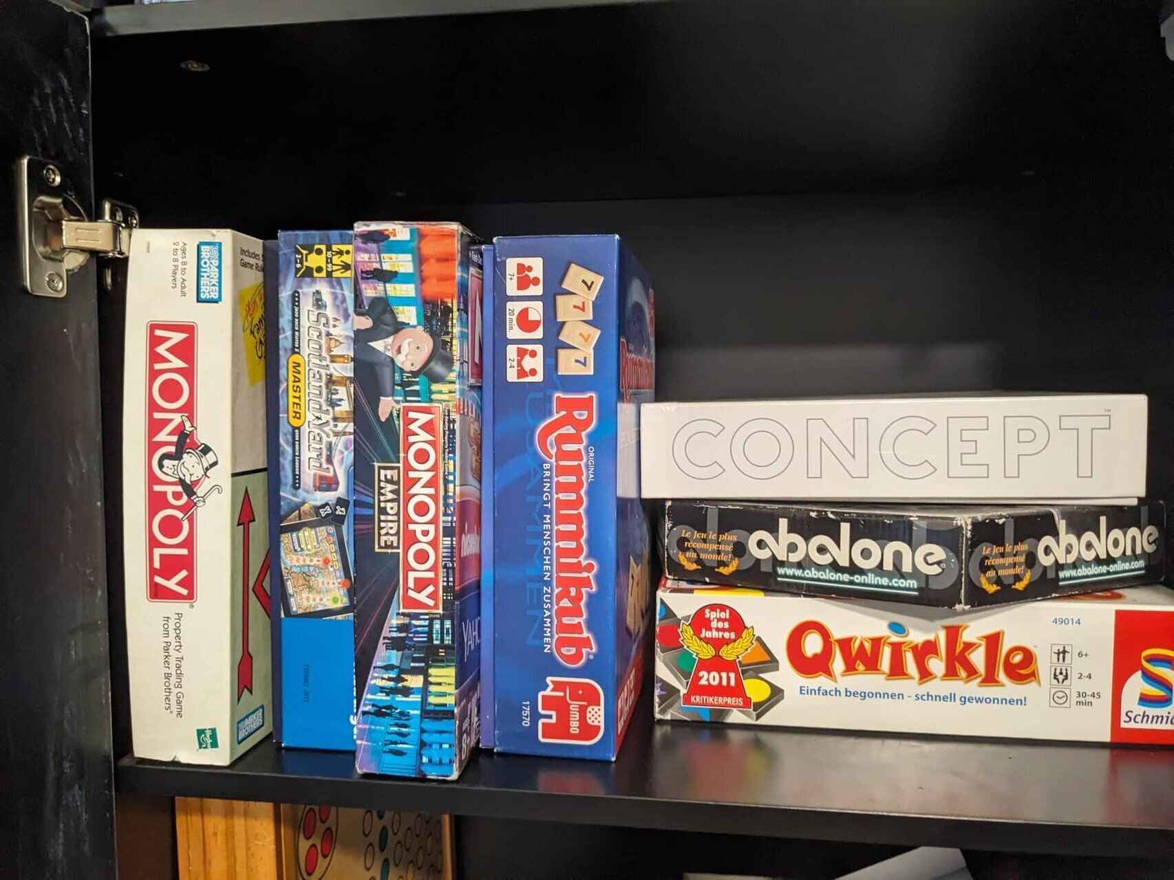 A shelf with various board games including Monopoly, Master, and Concept.