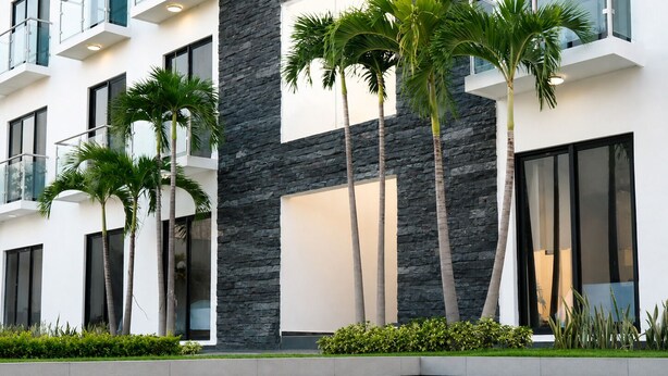 Un bâtiment moderne doté d’une piscine, d’une façade en pierre et de palmiers.