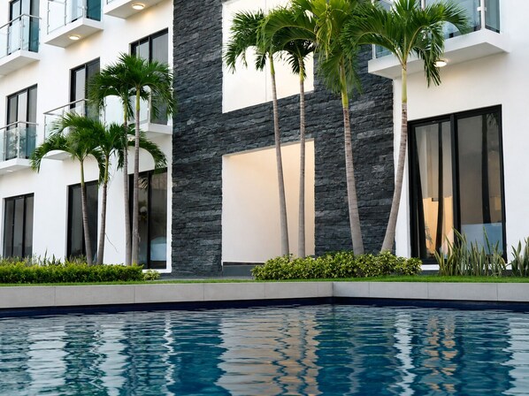 A modern building with a pool, stone facade, and palm trees.