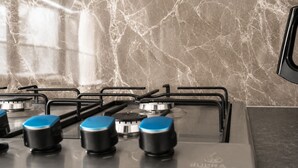 Une cuisine équipée d’une cuisinière à gaz, de poignées noires et d’un pare-feu en marbre.