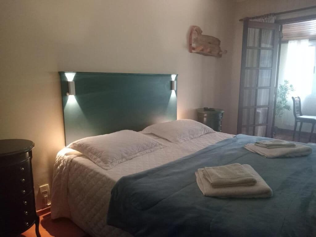 Een slaapkamer met een bed, een nachtkastje, een wandlamp en een raam met uitzicht.