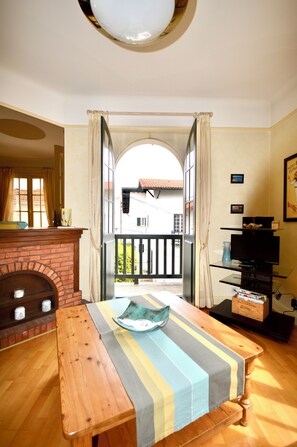 Ein Zimmer mit Holztisch, Kamin, Fernseher und Blick auf einen Balkon.