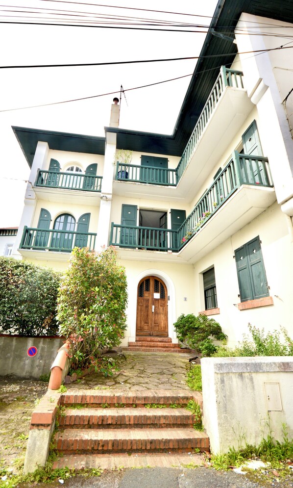 A two-story building with a wooden front door, a balcony on the second floor, and a staircase leading to the entrance. - Vrbo Property (Biarritz)